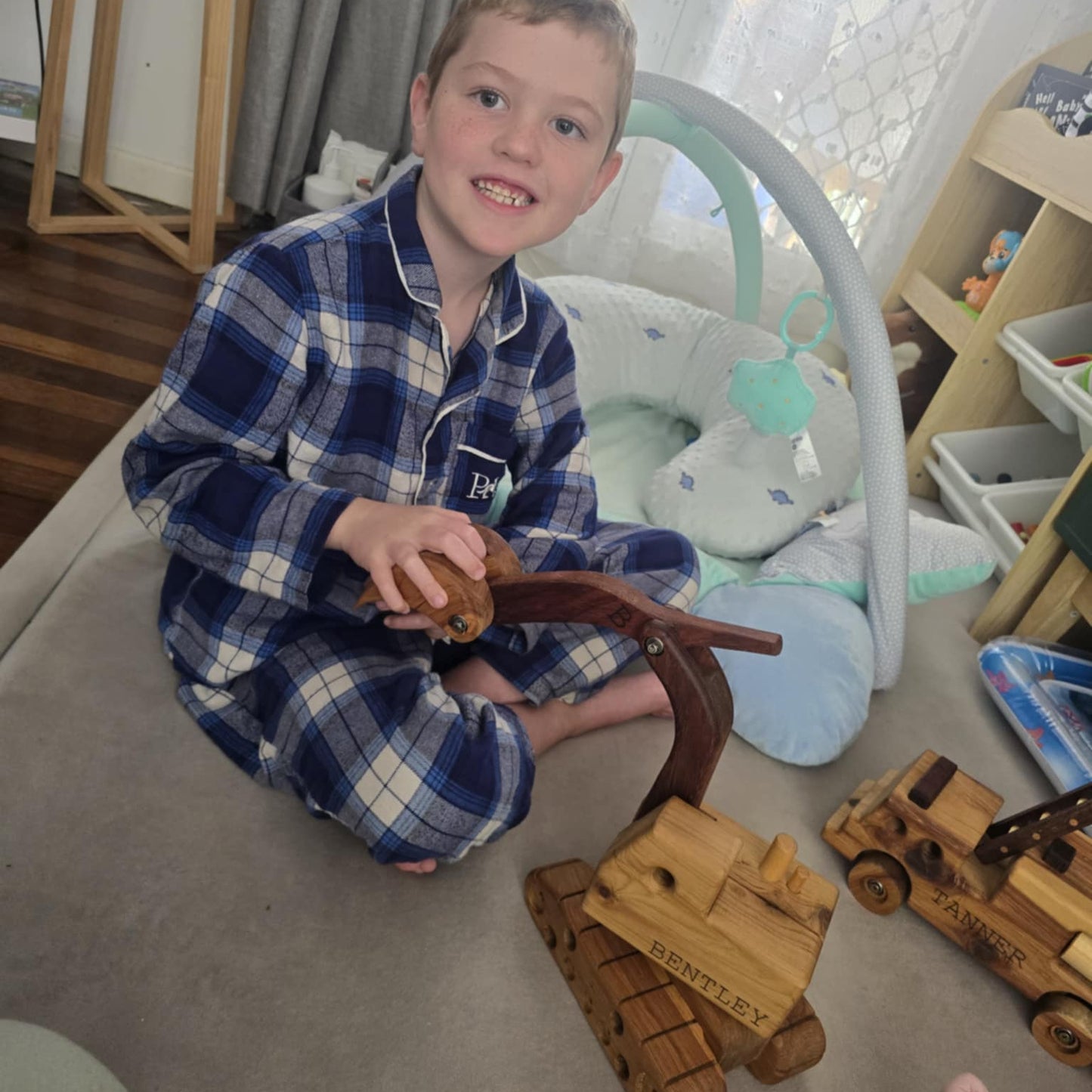 A 6 year old boy smiling at his gifted wooden digger with his name engraved on it.
