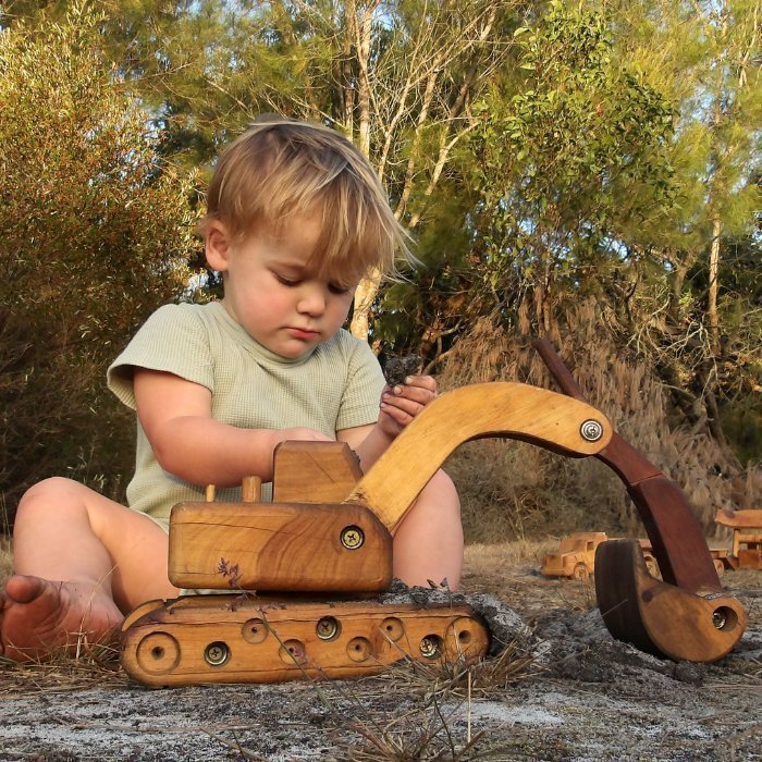 A young boy happily playing with Heirloom Handmade Wooden Excavator . Luxury, exclusive.