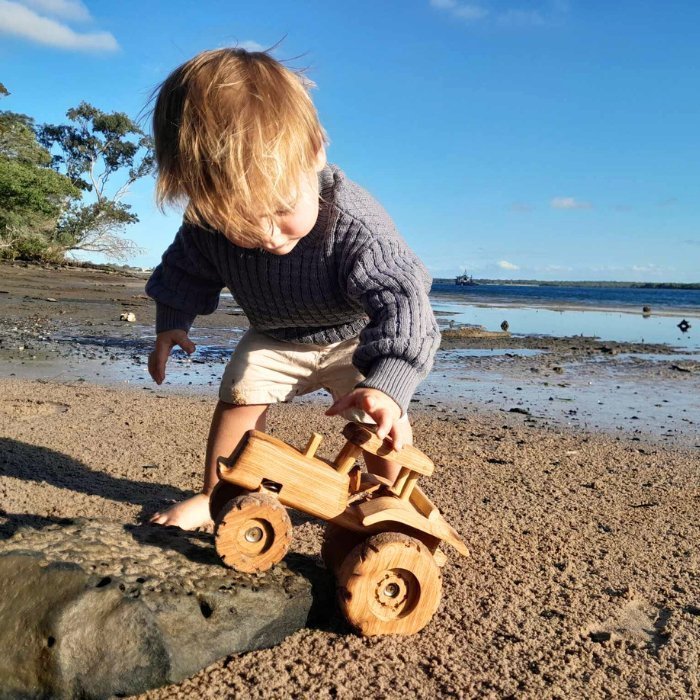 3 year old boy playing with handmade Wooden Tractor toy on Beach. Showcasing Suspension. Rolling Wheels. Durability and premium Quality.
