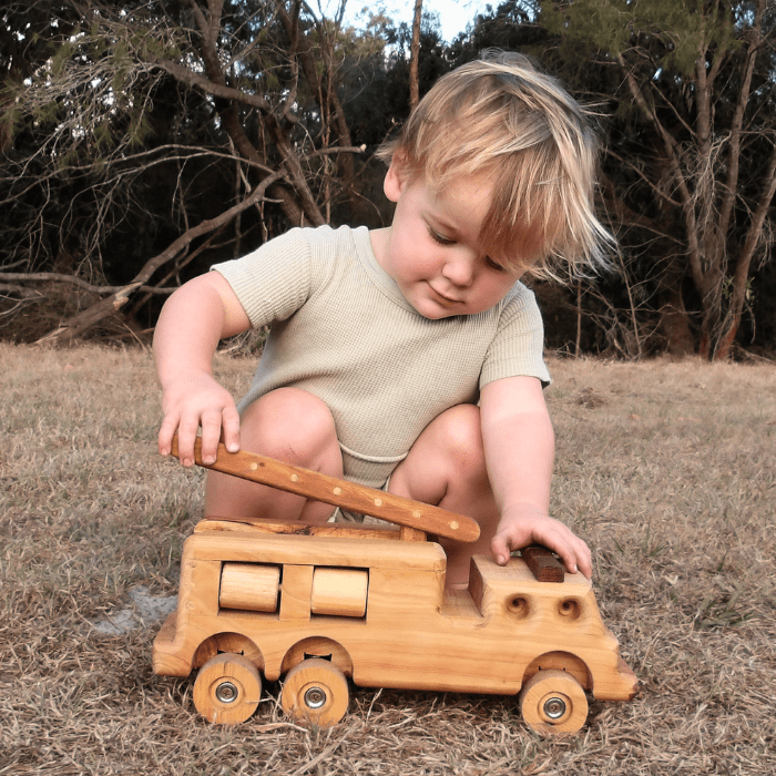 A young boy happily playing with Heirloom Handmade Wooden Fire Truck. Luxury, exclusive. 