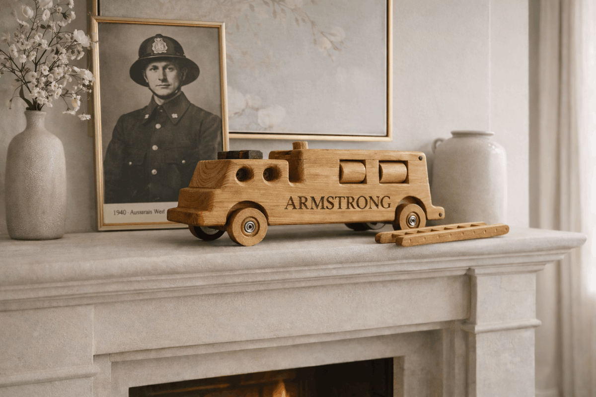 Handcrafted wooden firetruck heirloom engraved “ARMSTRONG” displayed on a cream stone fireplace mantel in an Australian farmhouse, with a vintage 1940s Australian firefighter portrait in the background.