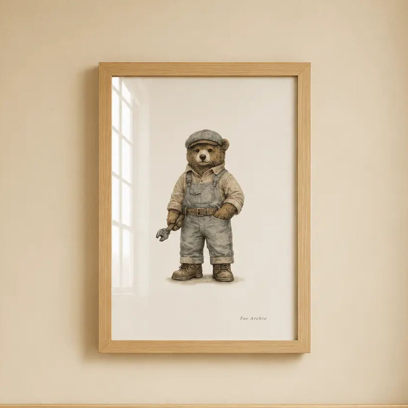 A framed art print of a teddy bear dressed as a Low Loader  worker hanging on a beige wall above a light wood crib.
