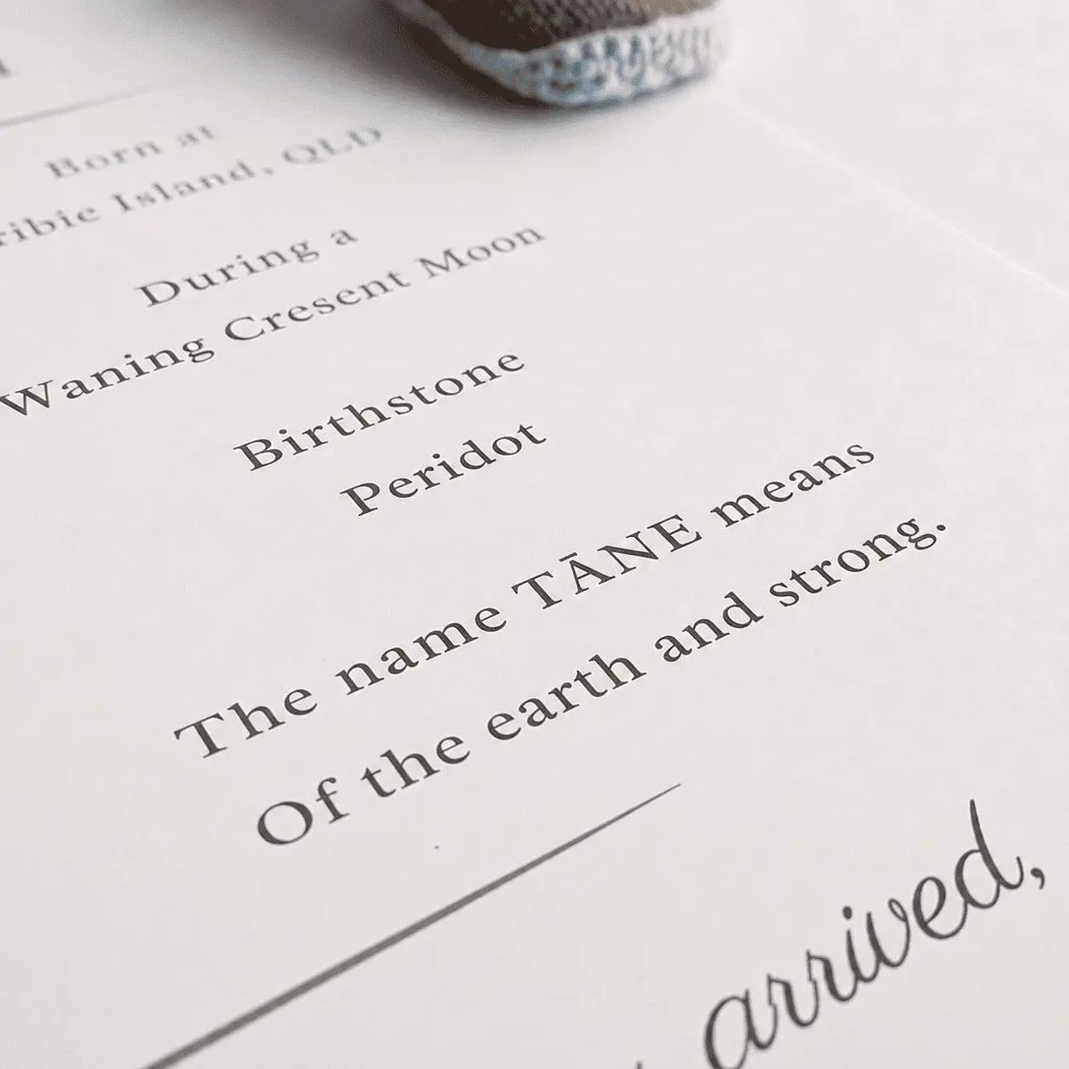 A close-up of a researched name meaning with elegant black serif text on white paper, partially overlaid by a textured gray and white shoe at the top edge.