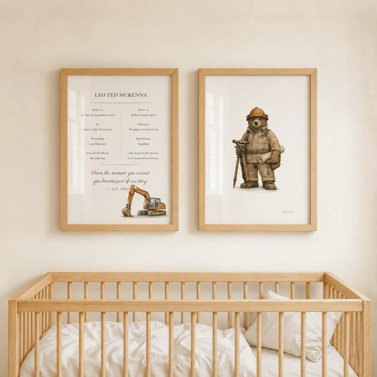 Two framed personalized firefighter-themed nursery prints hanging on a beige wall above a light wood crib. The left print is a custom birth chart for 'Leo Ted McKenna' with a small excavator illustration, and the right print shows a excavator bear holding an axe.