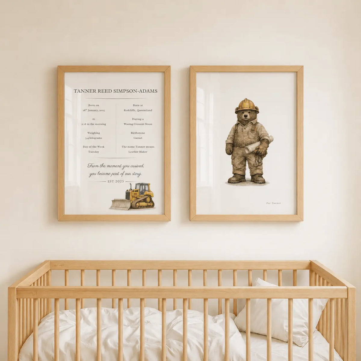 Two framed nursery wall prints hang above a light wood crib. The left print is a Tanner Reed Simpson-Adams birth chart with a small yellow construction bulldozer illustration.