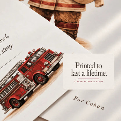 A close-up of printed archival paper featuring a red fire truck illustration and part of a firefighter uniform, with a white label reading 'Printed to last a lifetime. 210GSM ARCHIVAL GLOSS' and 'For Cohan'. fire truck